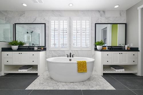 primary bath with freestanding bathtub, dual white vanities and marble tile wall at Plan 1 Dover at Compass Bay in Newark, California