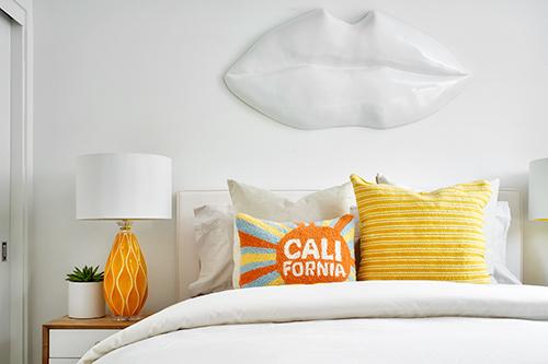 bed with yellow, orange, and light blue printed pillows The QUE