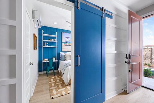 first floor bedroom with blue accent wall and blue barn door Townes at Magnolia Plan 2 Melia Homes