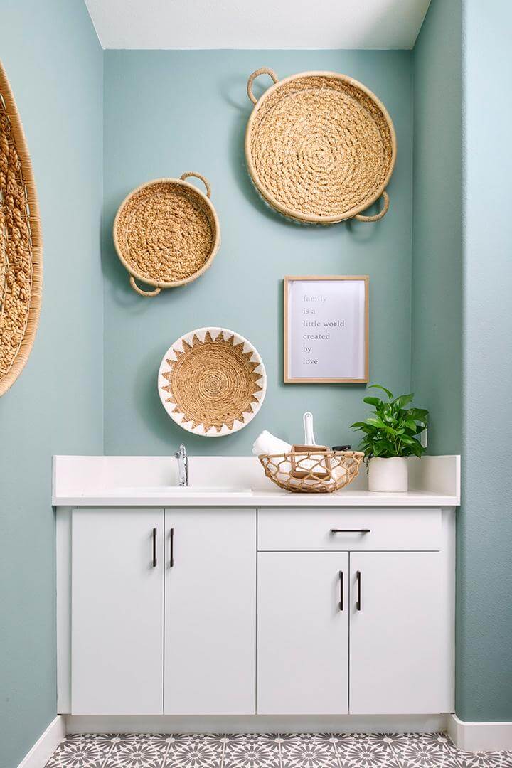 four woven baskets on light teal painted wall, white vanity with white countertop and backsplash, woven basket, potted plant, gray and white patterned floor tile in laundry room, PGA West