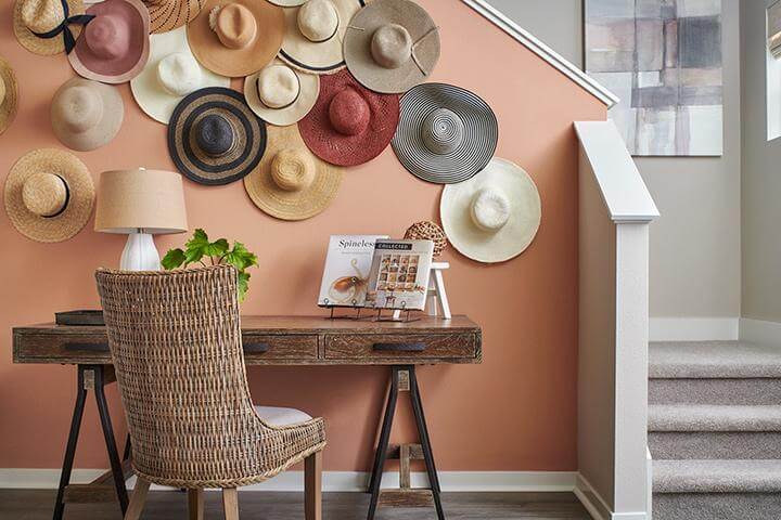 collection of multi-colored straw hats as wall decor, wood desk, table lamp, tray, potted plant, rattan chair in entryway, Verge