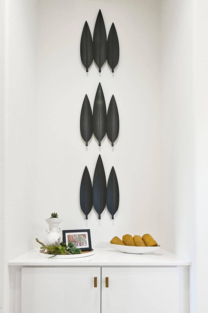 three sets of black leaf 3D wall art, white built-in cabinet, white bowl and tray with decorative accents, PGA West