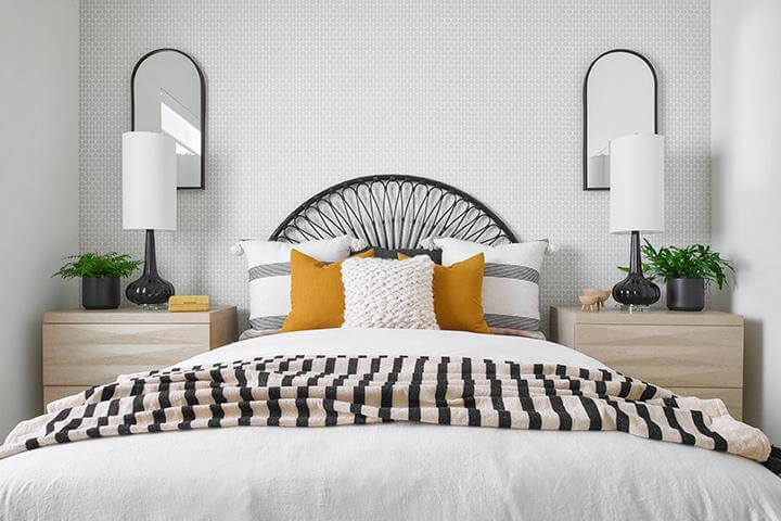 cream and white small patterned wallpaper, white bedding with mustard, gray, and white accent pillows, black and white striped blanket, birch bedside tables, black table lamps, two black framed mirrors in bedroom, PGA West