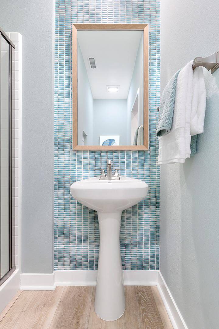 light blue and white tile look wallpaper, white pedestal sink, birchwood framed mirror in powder room Townes