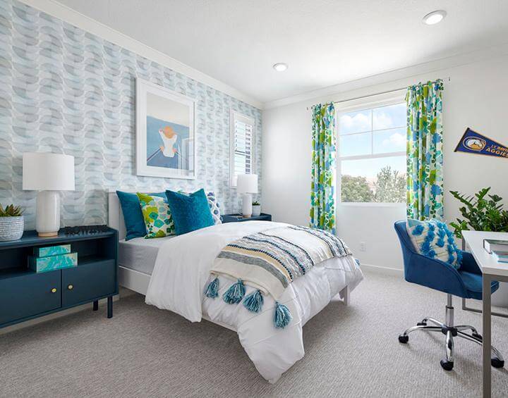 light blue and gray half circle patterned wallpaper, bed with white, cerulean blue and green bedding, cerulean bedside table and chair, patterned curtains in bedroom Splash at One Lake