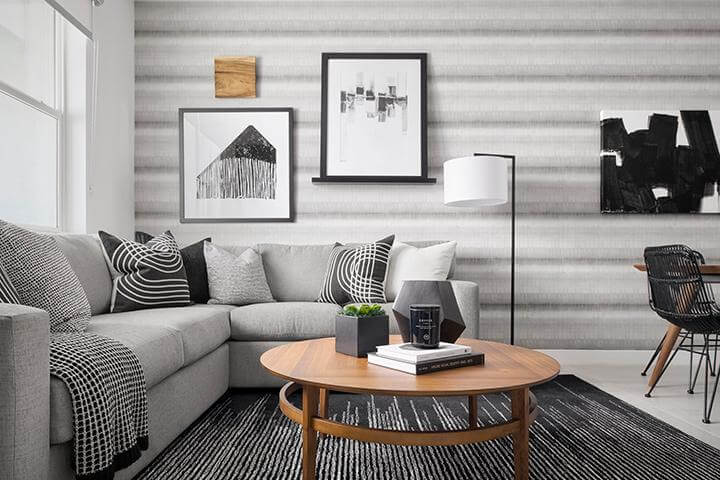 tonal gray blurred stripe wallpaper, gray sofa with black and gray pillows, wood coffee table, black floor lamp, black framed artwork in living room Townes