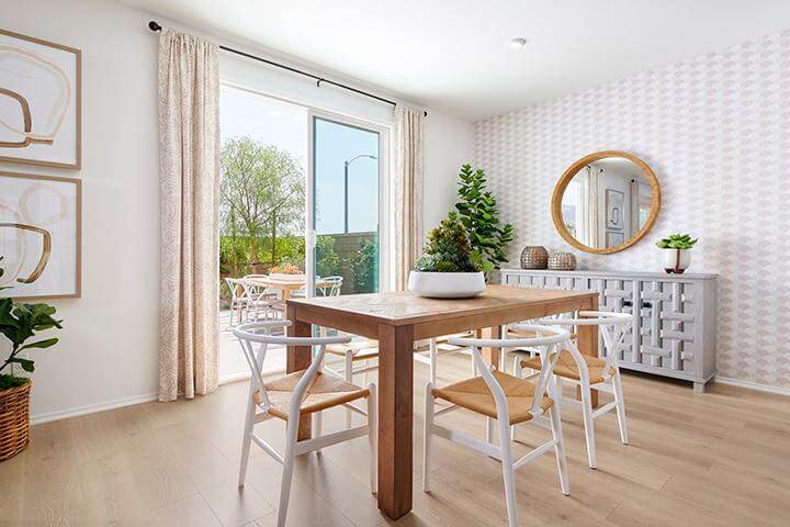 light honey triangle patterned wallpaper, wood dining table with rattan and white chairs, gray buffet table, wood framed circular mirror in dining room Rancho at Palma Navarra