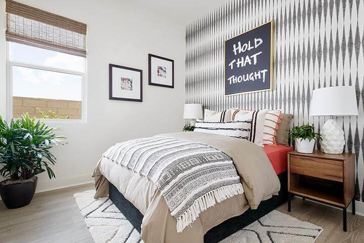 light gray elongated diamond patterned wallpaper, beige, black and white bedding, wood bedside table, quotable wall art, white and black patterned area rug in bedroom Revo