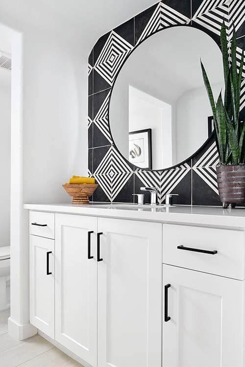 bathroom vanity with black and white tiled wall and circular mirror
