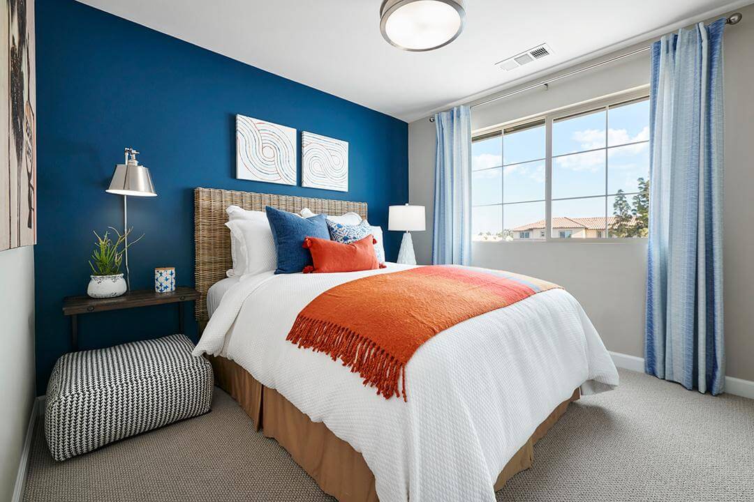 blue bedroom with orange throw blanket and pillows