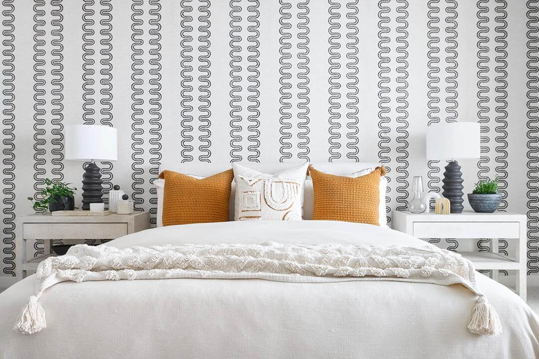 white bedroom with orange throw pillows and graphic wallpaper